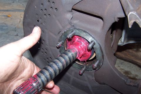 1990 Ford Bronco - Close-up of a greased axle shaft and brake rotor assembly, with a hand present.