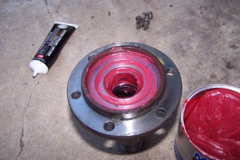 1990 Ford Bronco - Wheel hub assembly being greased with assembly lube and red grease, with small nuts in the background.