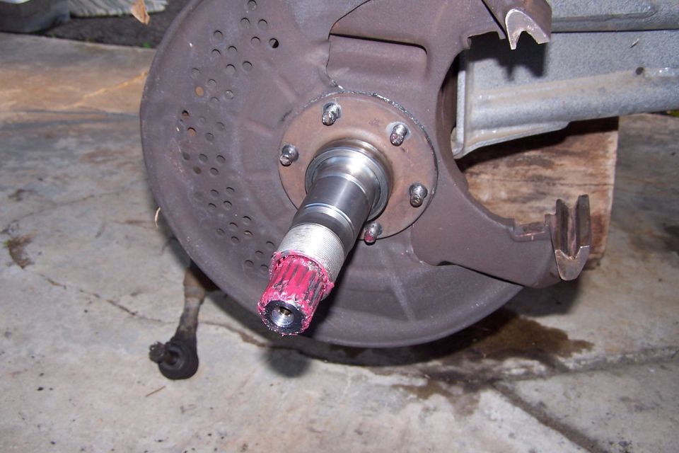 Close-up of a vehicle's wheel hub assembly, showing the spindle with red grease applied