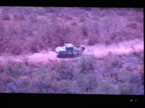 1986 Ford Bronco - Off-road vehicle driving on a dusty dirt road through a wooded area.