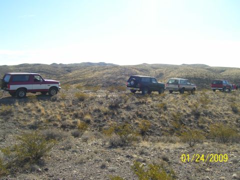 1993 Ford Bronco - Four Ford Broncos are parked on a desert hill. The lead vehicle is a two-tone red and white model.