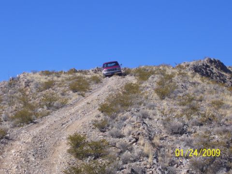 1993 Ford Bronco - A red SUV navigates a steep, rocky incline on a clear day.