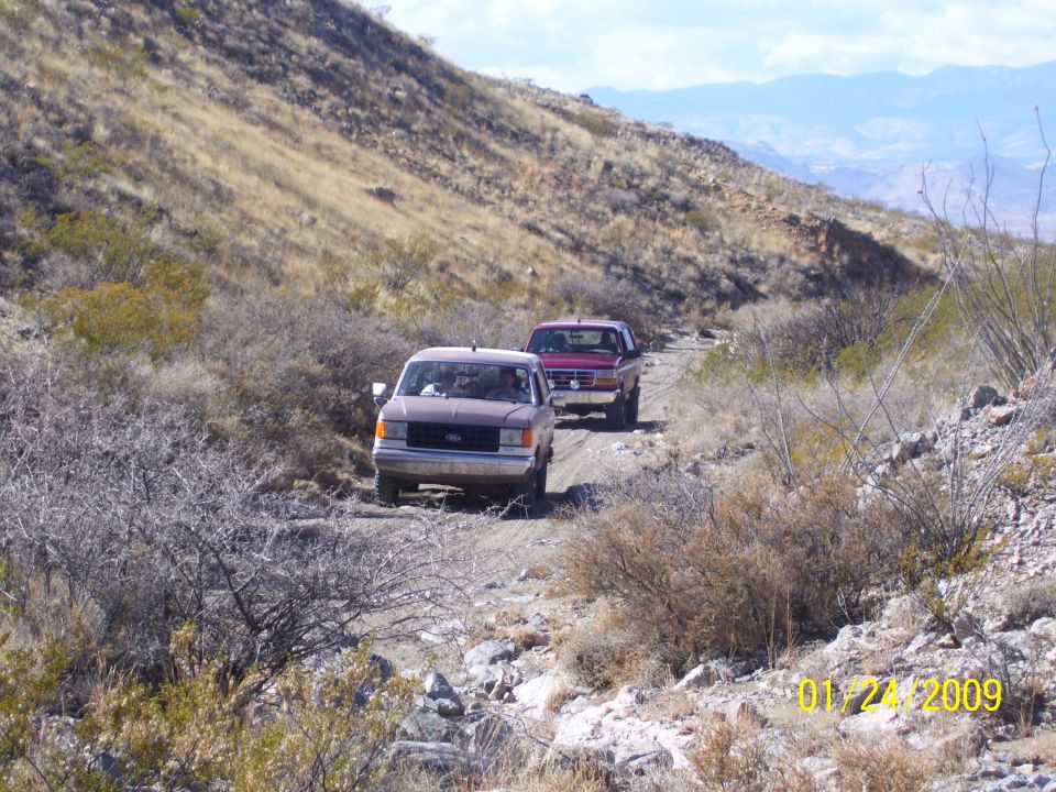 1993 Ford Bronco and a Ford pickup truck on a dirt road in a desert landscape