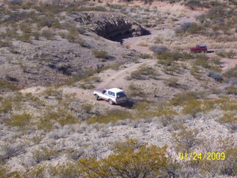 1993 Ford Bronco - Two SUVs navigate a dusty trail through a rocky, arid terrain under a clear sky.