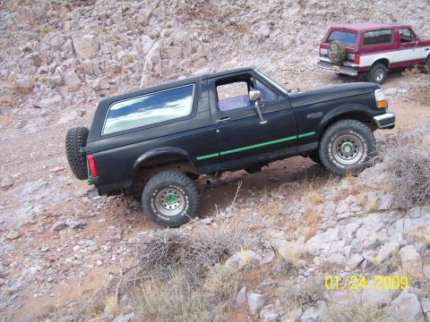 1993 Ford Bronco - A black 1993 Ford Bronco navigates rocky terrain, with a second Bronco visible in the background.