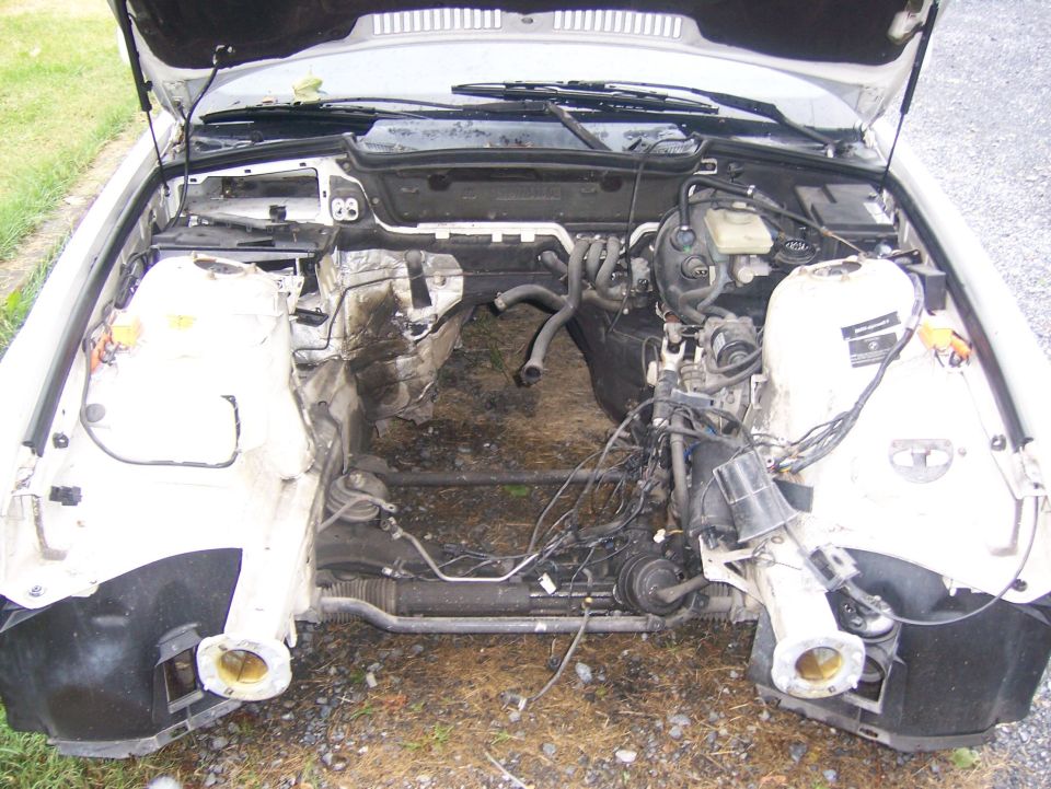 Engine bay of a white BMW with hood open, engine removed