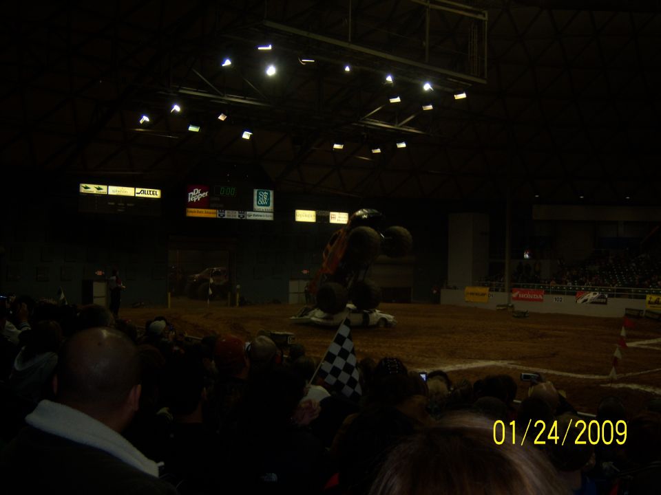 Monster truck jumping over a car in an arena, with a crowd watching