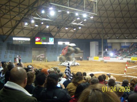 1996 Ford Bronco - A monster truck soars through the air over a pile of cars during a show, with spectators watching from the stands.