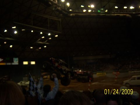 1996 Ford Bronco - Monster truck show with two trucks in action and a crowd watching.