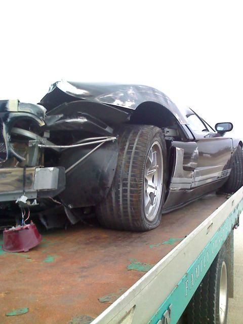 1992 Ford Bronco - A black sports car with significant rear-end damage is loaded onto a tow truck.