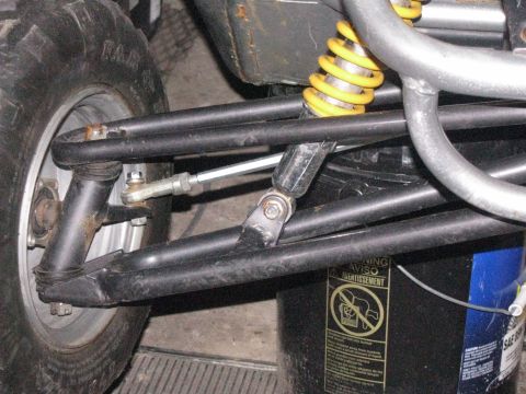 2006 Ford F1 - Close-up of go-kart rear suspension components and a tire, with a warning label on a bucket in the background.