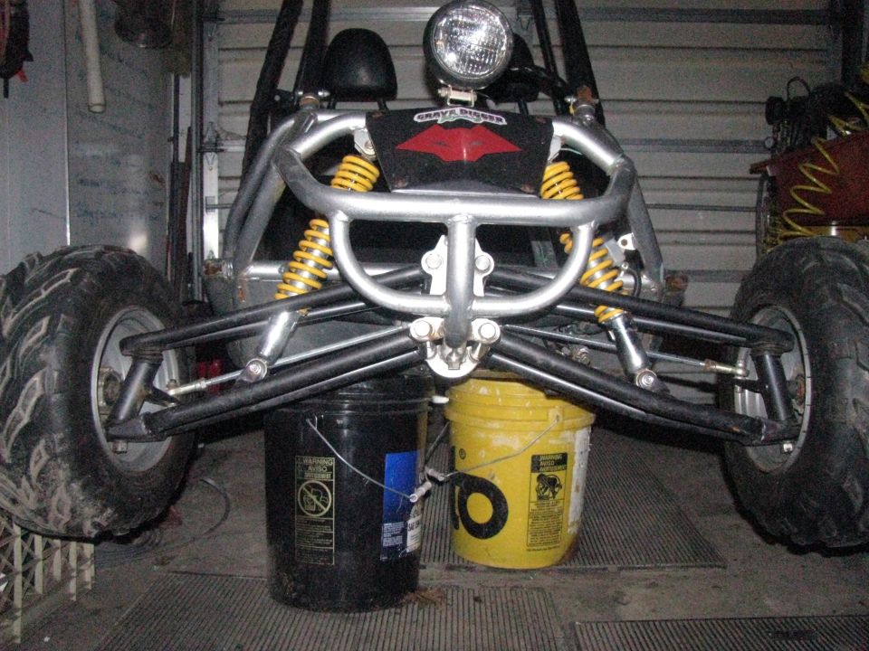 Tube-frame off-road go-kart front end on buckets showing A-arms, yellow coilovers and knobby tires