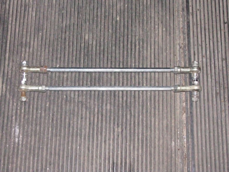 Two metal rods with threaded ends and ball joints, laid out horizontally on a ribbed surface
