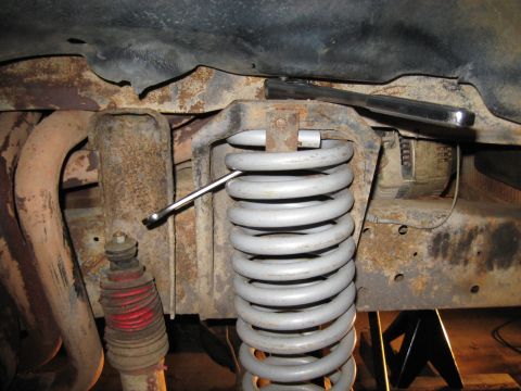 1978 Ford Bronco - Close-up view of a vehicle's suspension system, showing a coil spring and shock absorber with a wrench engaged on a bolt.