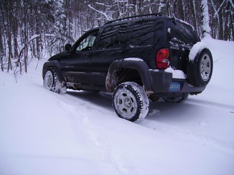 2000 Chevrolet Tahoe - A black Jeep Liberty navigates a snowy forest road, its tires kicking up snow.