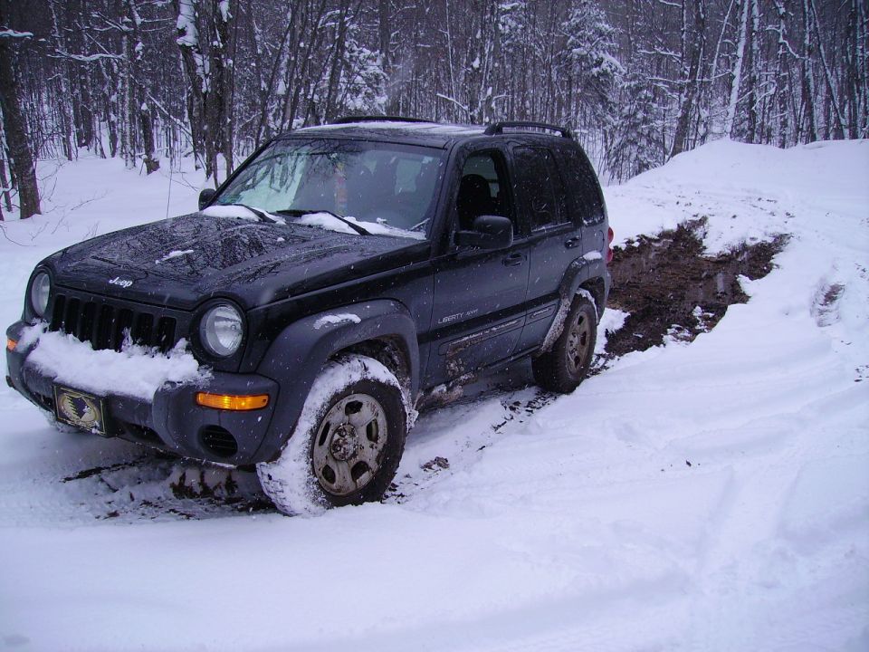 Black Jeep Liberty stuck in a snowy ditch, front wheel deep in mud