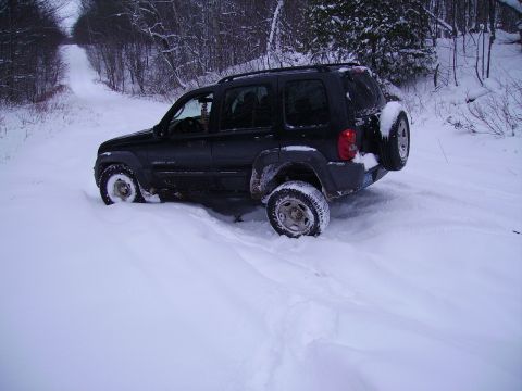 2000 Chevrolet Tahoe - A black Jeep Liberty is stuck in the snow on a rural road, with trees lining the path.