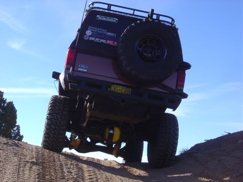 1996 Ford F-250 - This lifted Ford Bronco is equipped with a spare tire and off-road stickers, seen climbing a dirt incline.