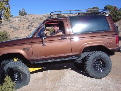 1996 Ford F-250 - A man drives a lifted Ford Bronco II on a dirt trail under a clear blue sky.