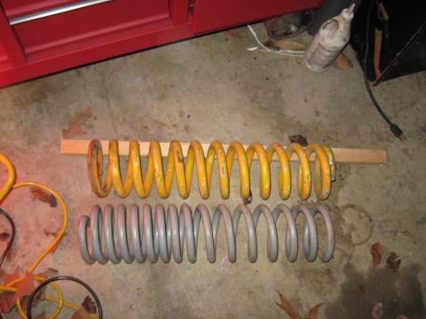 1978 Ford Bronco - Comparison of two different coil springs, one yellow and one gray, resting on a wooden plank.