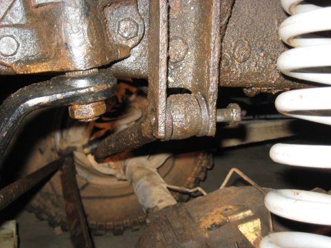 1978 Ford Bronco - Close-up of heavily rusted vehicle suspension components, including a linkage and a white coil spring.