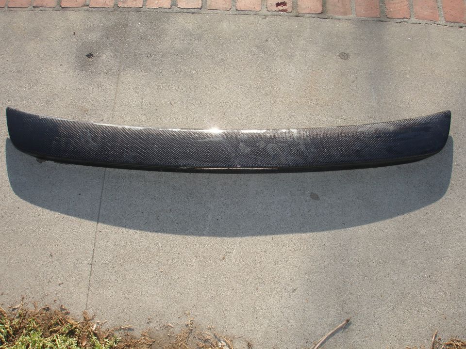 Carbon fiber rear trunk spoiler lying face-up on a concrete driveway