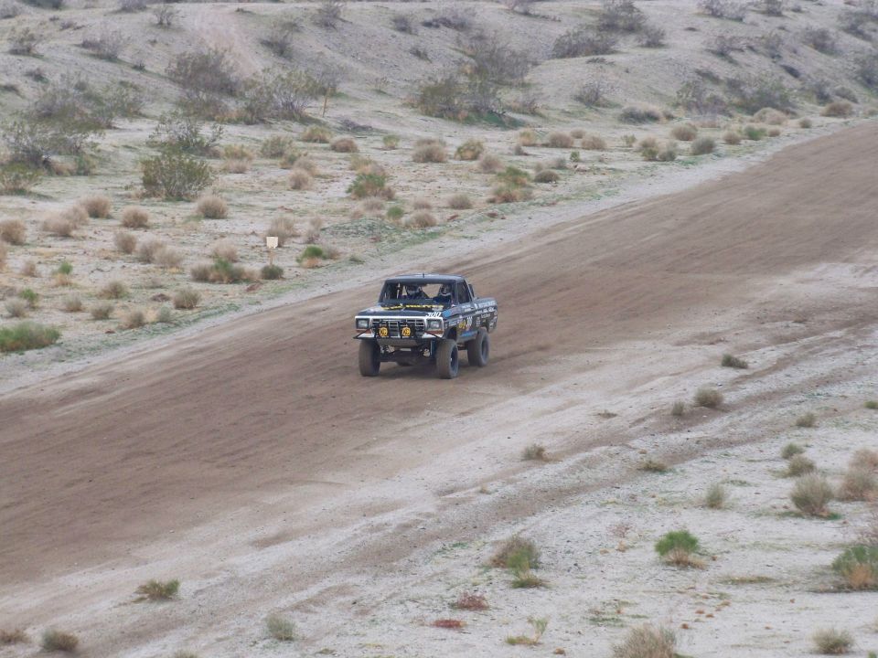 Off-road race truck driving on a dirt track in a desert landscape