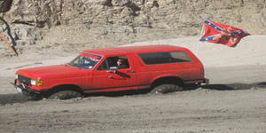 1987 Ford Bronco - Red 1987 Ford Bronco stuck in sand, Confederate flag visible in background.