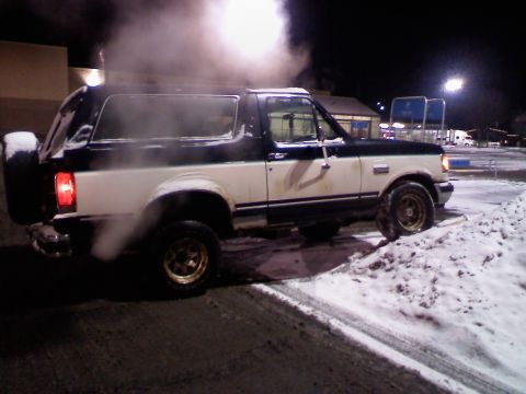 1988 Ford Bronco - A two-tone Ford Bronco is seen in a snowy environment, with smoke coming from its exhaust and engine area.