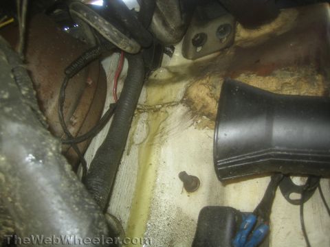 1990 Ford Bronco - grimy underbody or floorpan area showing wiring harnesses, a black rubber boot, hoses and a bolt with surface contamination.