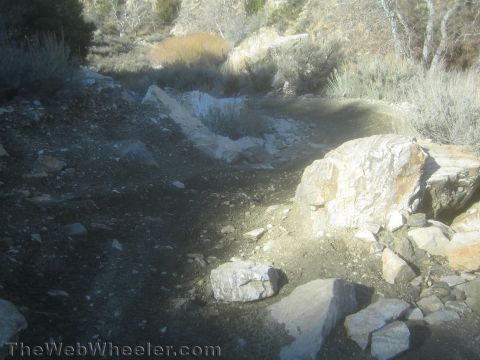 1990 Ford Bronco - rugged dry wash trail strewn with large pale boulders and sagebrush winding through a sunlit high-desert canyon.