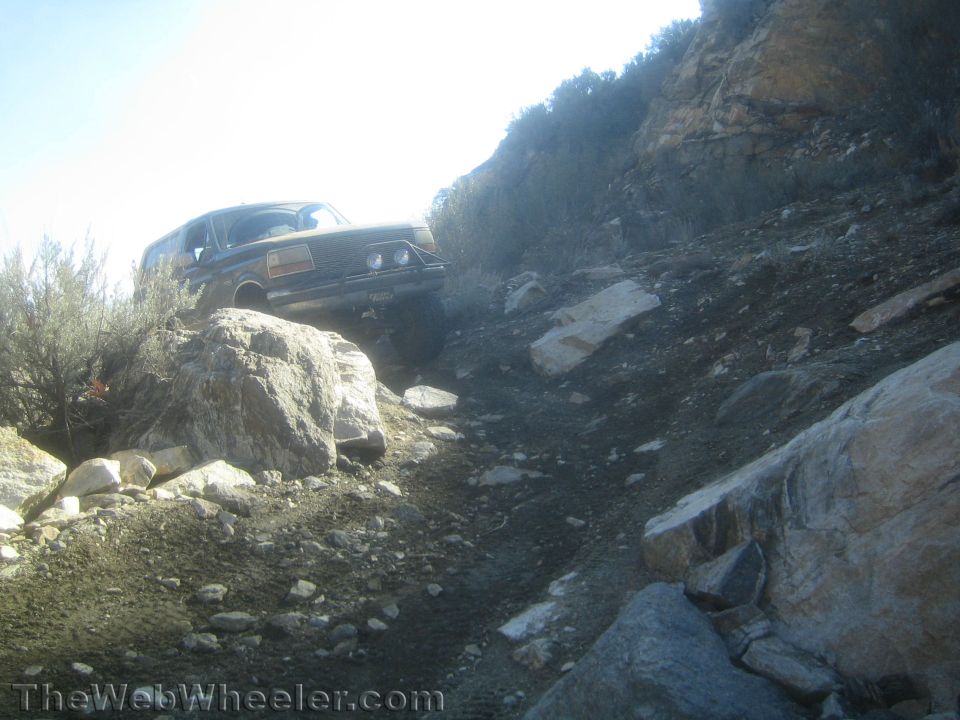 Dark SUV perched on rocks at the top of a steep rocky off-road climb