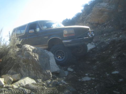 1990 Ford Bronco - lifted two-tone Ford Bronco flexes its suspension as it crawls over large rocks on a steep dirt-and-rock hillside trail.