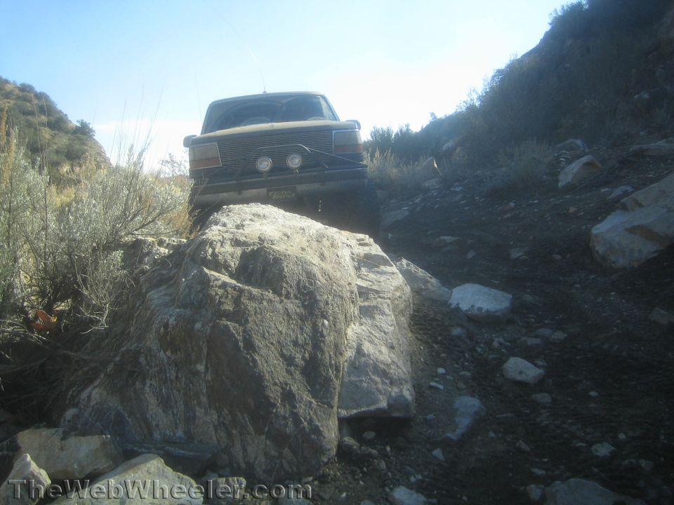 Front view of a lifted Ford Bronco cresting a large boulder on a rocky trail