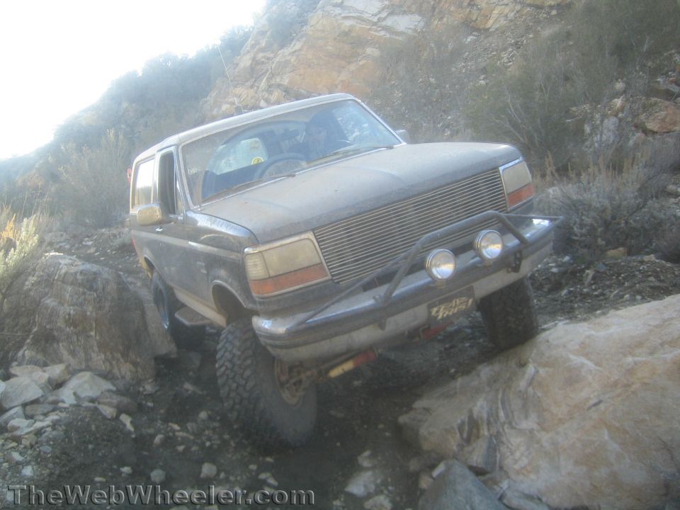 Muddy lifted Ford Bronco with billet grille and KC lights crawling rocks