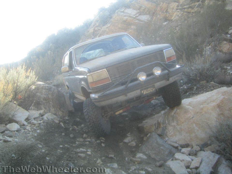 Lifted Ford Bronco with billet grille articulating over rocks on a steep trail