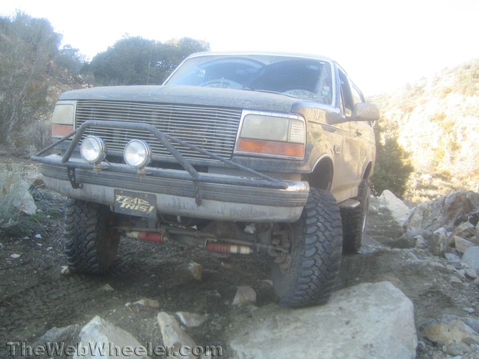 Front view of a dusty lifted Ford Bronco with brush guard and KC lights on rocks