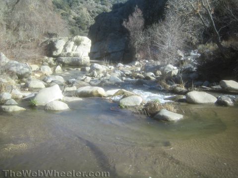 1990 Ford Bronco - shallow stream flows over and around scattered boulders through a sunlit canyon with bare winter trees.