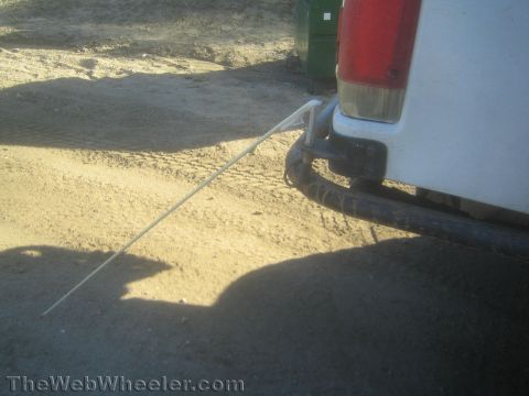 1990 Ford Bronco - Close-up of a white truck's rear bumper and red taillight with a thin antenna cable trailing across dirt ground.