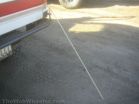 1990 Ford Bronco - rear of a red-and-white truck with a step bumper and license plate, a taut cable stretching across the dirt lot.