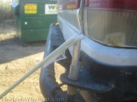 1990 Ford Bronco - Close-up of a dusty white truck's rear bumper and taillight with a frayed wire, a green dumpster in the background.