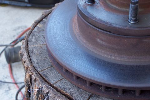 1990 Ford Bronco - Rusted brake rotor assembly on a log, likely awaiting replacement or repair.