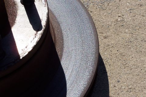 1990 Ford Bronco - A close-up view of a worn brake rotor resting on a gravel surface.