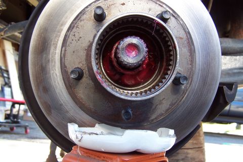 1990 Ford Bronco - Front brake rotor and hub with exposed splined spindle and red grease on the axle nut, vehicle on jack stands.
