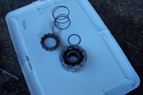 1990 Ford Bronco - Several metal automotive parts, including a gear and a ring assembly, are laid out with black o-rings on a white plastic surface.