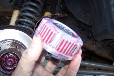 1990 Ford Bronco - A close-up shows a greased hub assembly part being held, with the vehicle's suspension and brake components in the background.