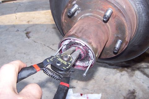 1990 Ford Bronco - A close-up shows snap ring pliers being used to remove a component from a vehicle's wheel hub assembly.