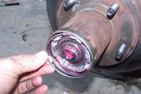 1990 Ford Bronco - A mechanic's hand holds a ring near a greased wheel hub assembly, suggesting maintenance or repair work.