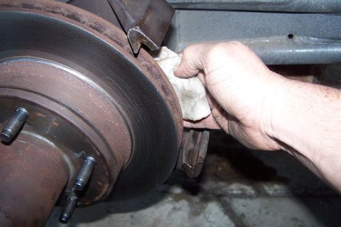 1990 Ford Bronco - A hand cleans a rusty brake rotor with a cloth, likely as part of maintenance.