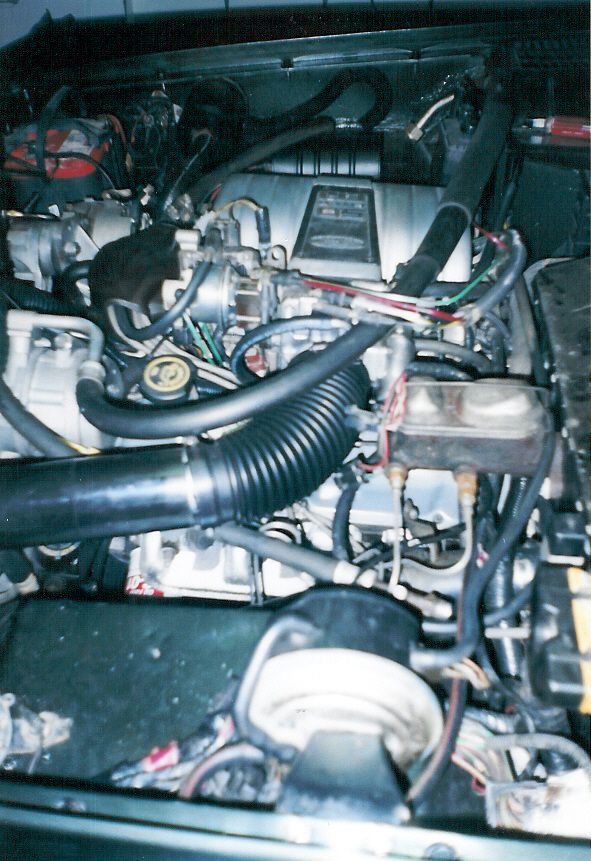 Crown Vic intake with a fabricated intake tube.  The original truck vacuum & wiring harnesses have been rearranged.  The IAC had to be flipped to clear the brake MC, and a throttle heater nipple had to be moved to clear the flipped IAC.  The vacuum cruise servo is in the foreground, and all the original '88 emissions equipment is in the background.